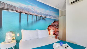 A hotel room with a bed, a nightstand, a lamp, and a view of a pier over water. - Darwin FreeSpirit Resort (Holtze)