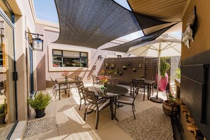 An outdoor patio area with a table and chairs, a large umbrella, and potted plants.