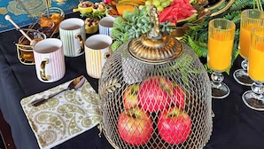 A table with various fruits, vegetables, and drinks, surrounded by decorative items and a small statue. - SW1 Lodge (Cape Town)