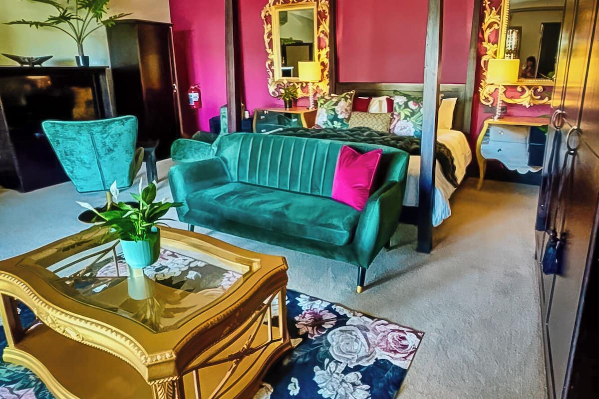 A living room with a green sofa, a wooden coffee table with a floral rug, a ceiling fan, and a red accent wall.