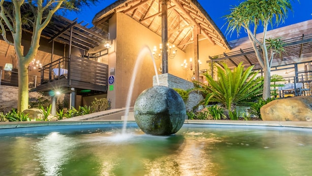 A pool with a spherical fountain, a building with a thatched roof, and surrounding greenery. - SW1 Lodge (Cape Town)