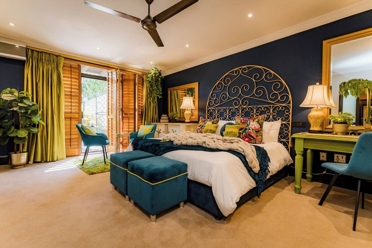 A bedroom with a large bed, a desk, and a chair. There is a ceiling fan and a window with curtains.