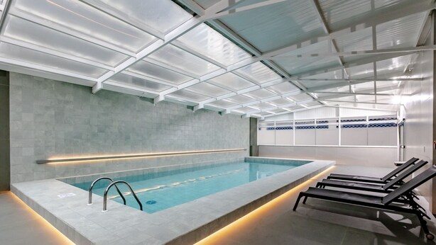 A modern indoor swimming pool with a clear water view, a tiled wall, and a ceiling with a grid pattern.