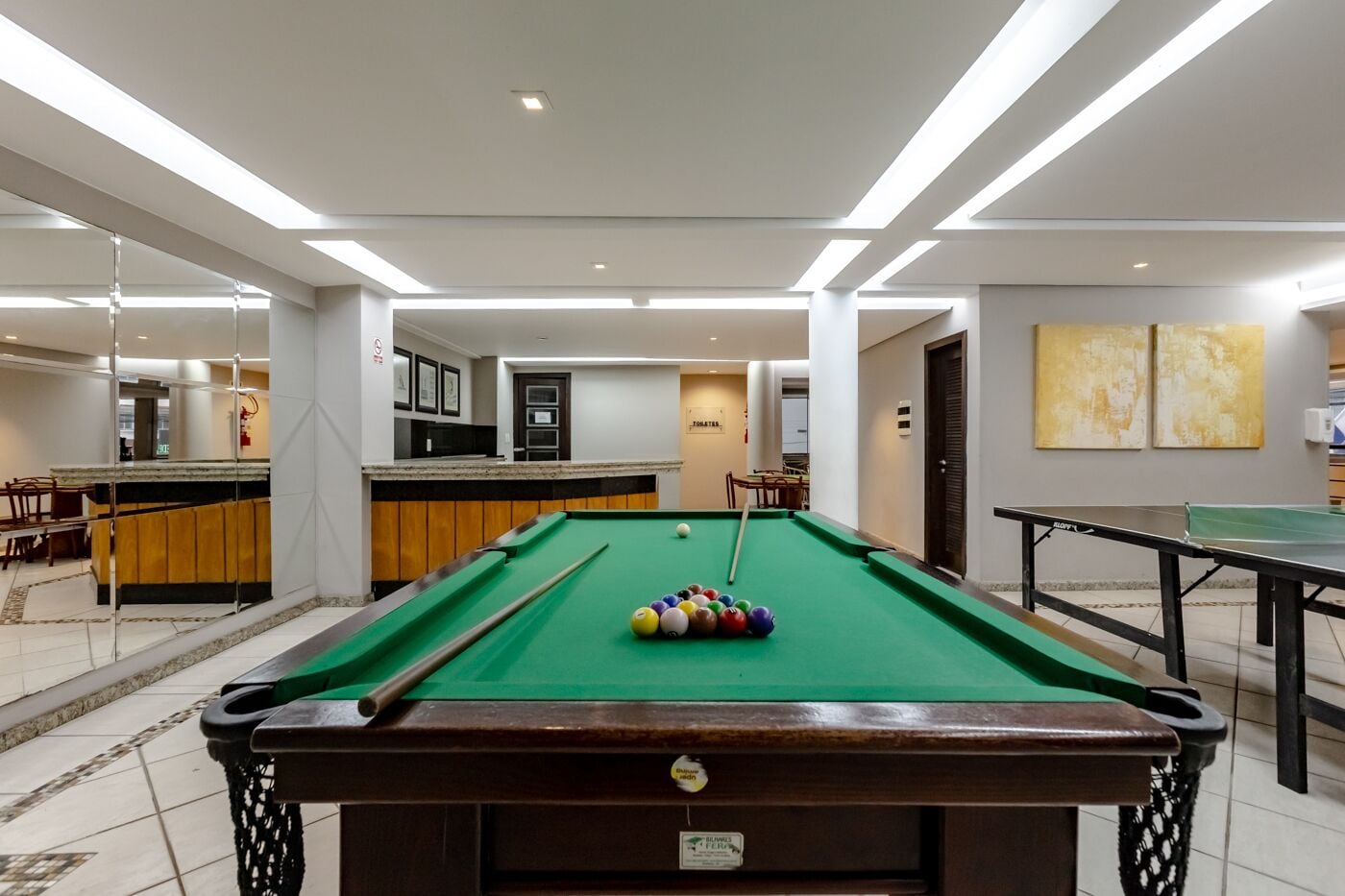 A pool table with balls, a billiards table, and a kitchen area with a counter and chairs.