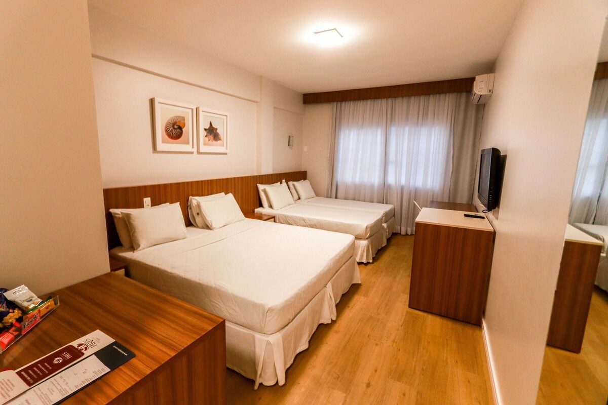 A hotel room with two beds, a wooden desk, a television, and a window with curtains.