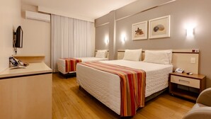 A hotel room with two beds, a desk, a telephone, and a wall-mounted air conditioner.