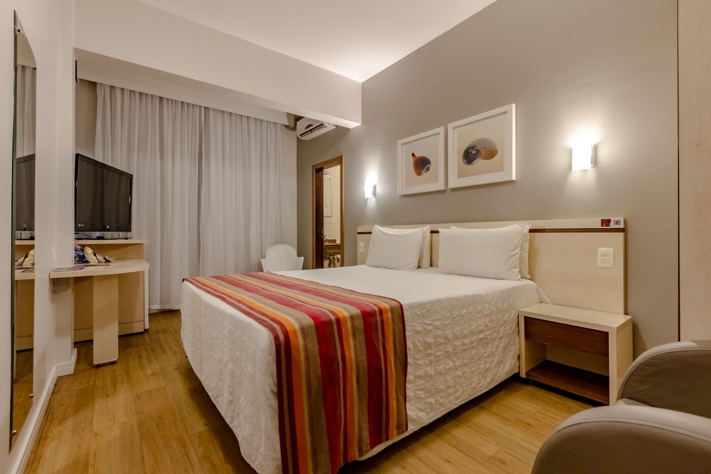 Een hotelkamer met een bed, bureau, televisie en kunst aan de muur.