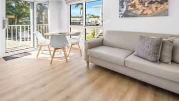 Ein modernes Wohnzimmer mit einer Couch, einem Esstisch mit Stühlen und großen Fenstern mit Blick ins Freie.