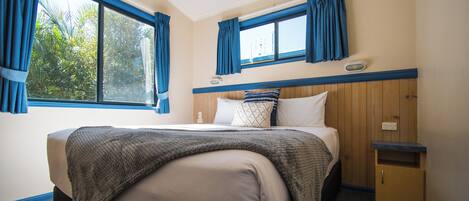 A bedroom with a large bed, a wooden headboard, a nightstand, and a window with curtains.