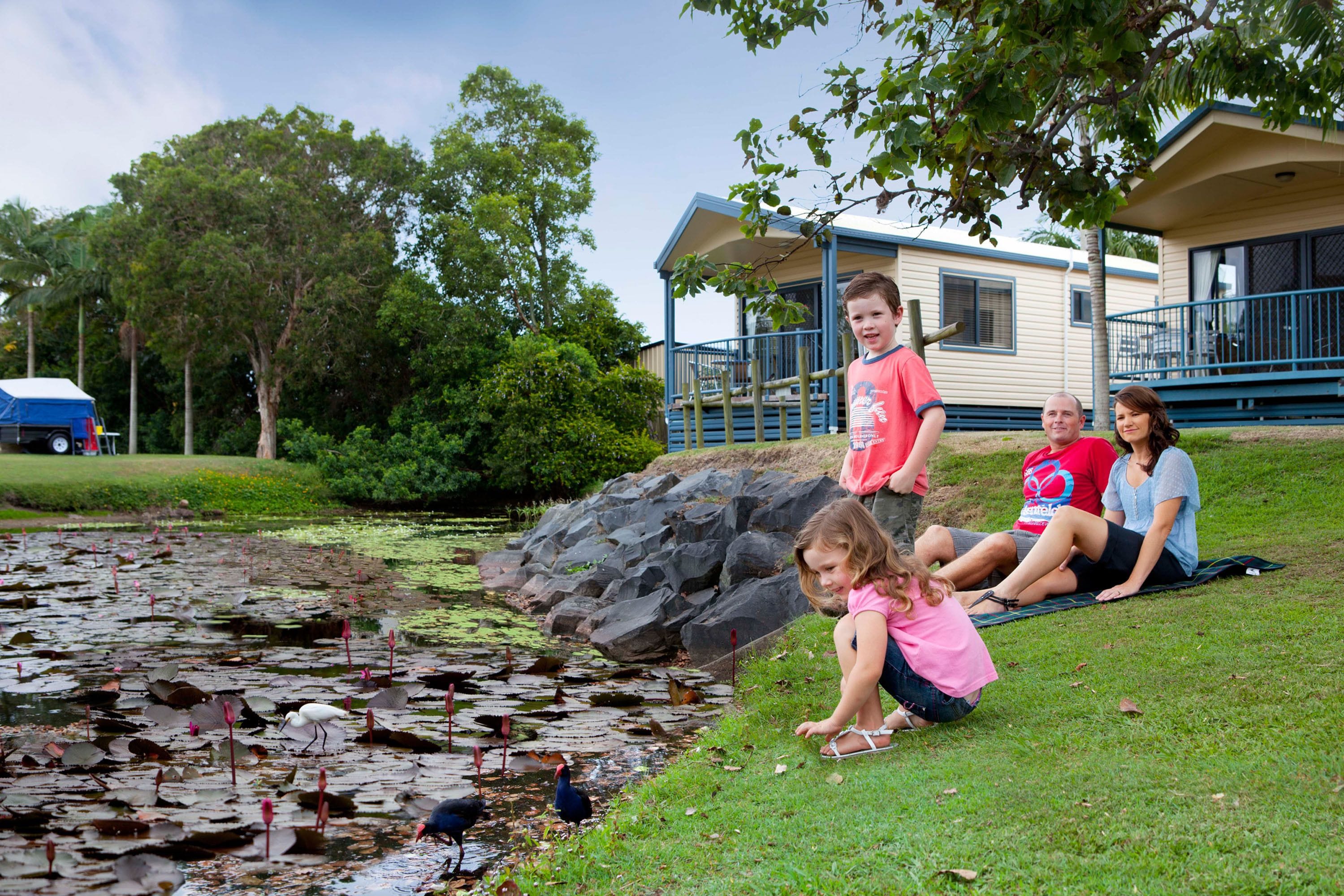 A family by a pond with ducks, a mobile home, and a blue deck.