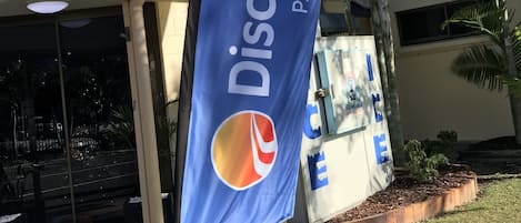 Señal de Discovery Parks con el logotipo de Pepsi, un edificio de fachada azul y beige, y palmeras al fondo.