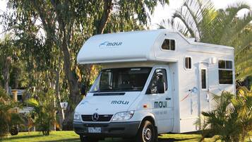 A white motorhome with the brand 'maui' parked in a grassy area with trees and a clear sky.