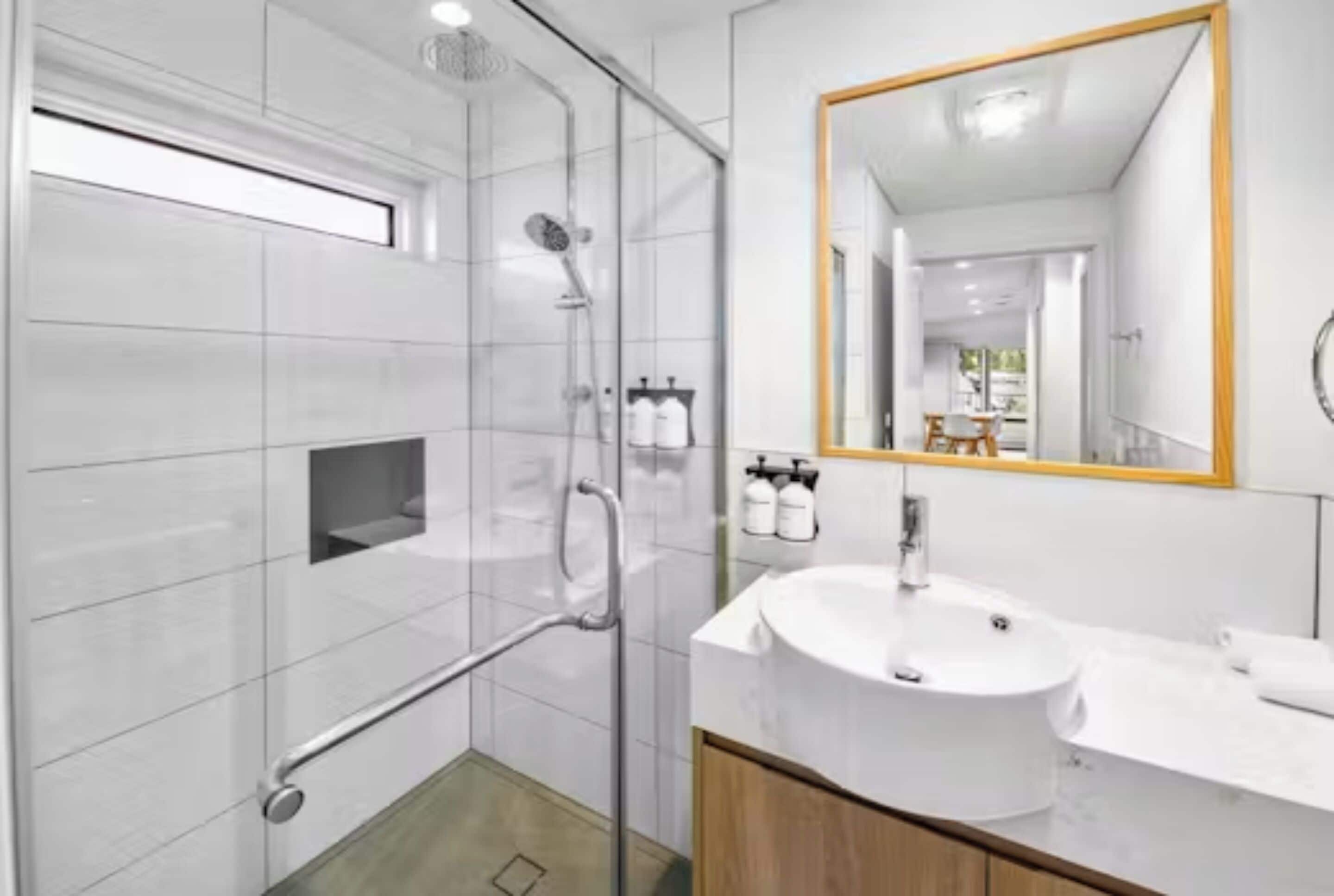 Une salle de bain moderne avec une douche à parois de verre, un lavabo blanc et un grand miroir.