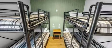 Un dormitorio con literas, tres camas literas, una mesita de madera y pared verde.