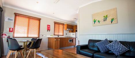 A modern living room with a wooden dining table, black leather sofa, and a kitchen in the background.