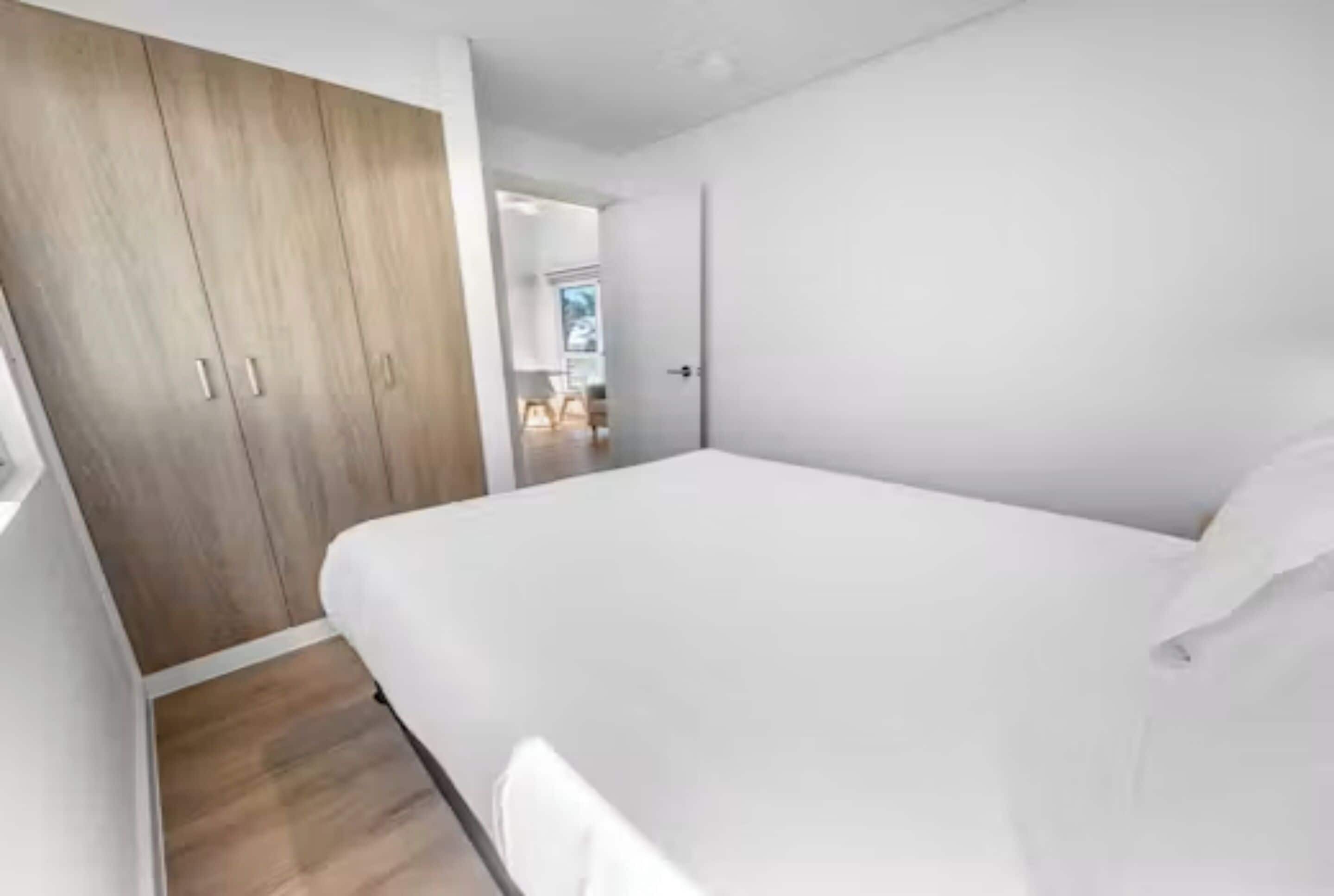 A bedroom with a wooden wardrobe, a bed, and a view of the outside.
