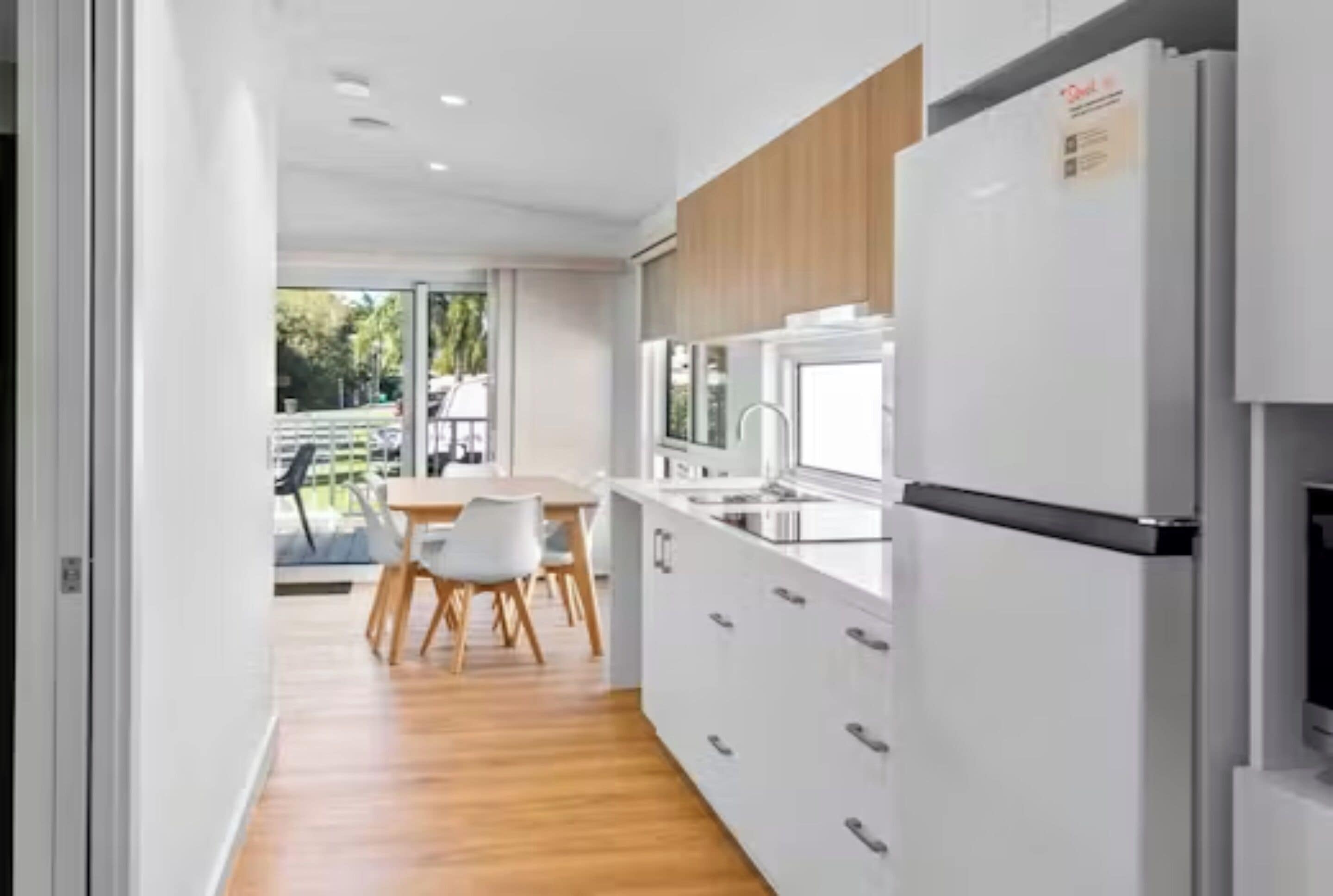 Una cocina moderna con armarios blancos, un refrigerador de acero inoxidable y un comedor con mesa y sillas.