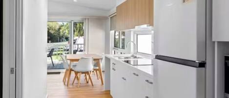 A modern kitchen with white cabinets, a stainless steel refrigerator, and a dining area with a table and chairs.