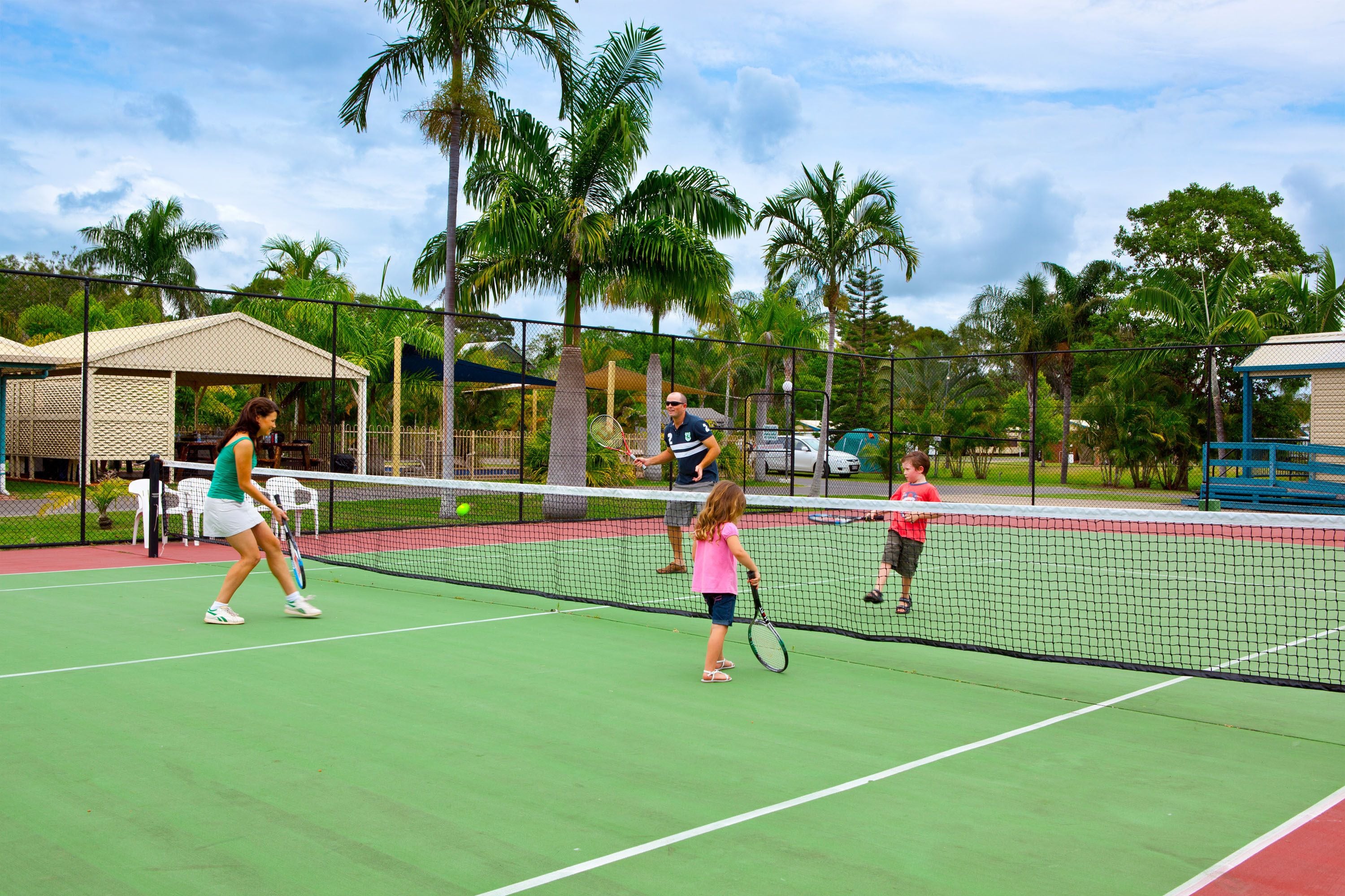 A tennis court with players, a net, and palm trees in the background.