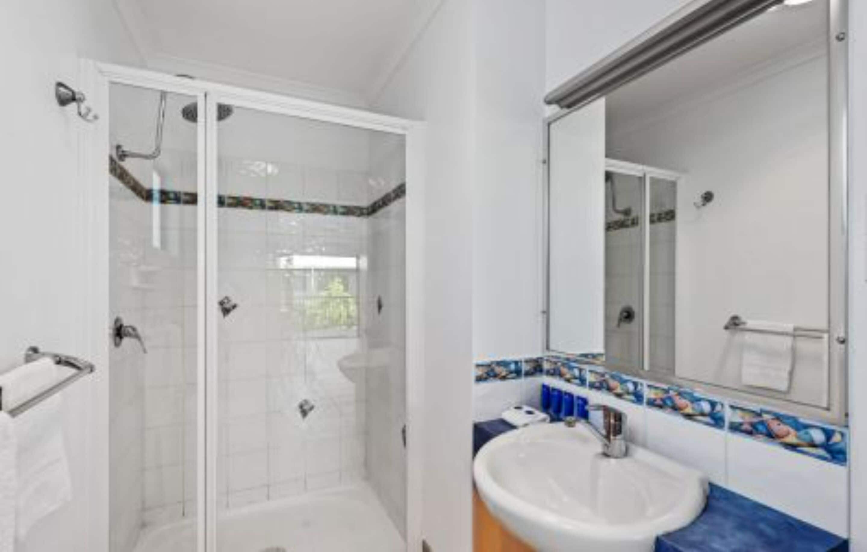 Un baño con ducha de vidrio, un lavamanos blanco y un salpicadero de azulejos.