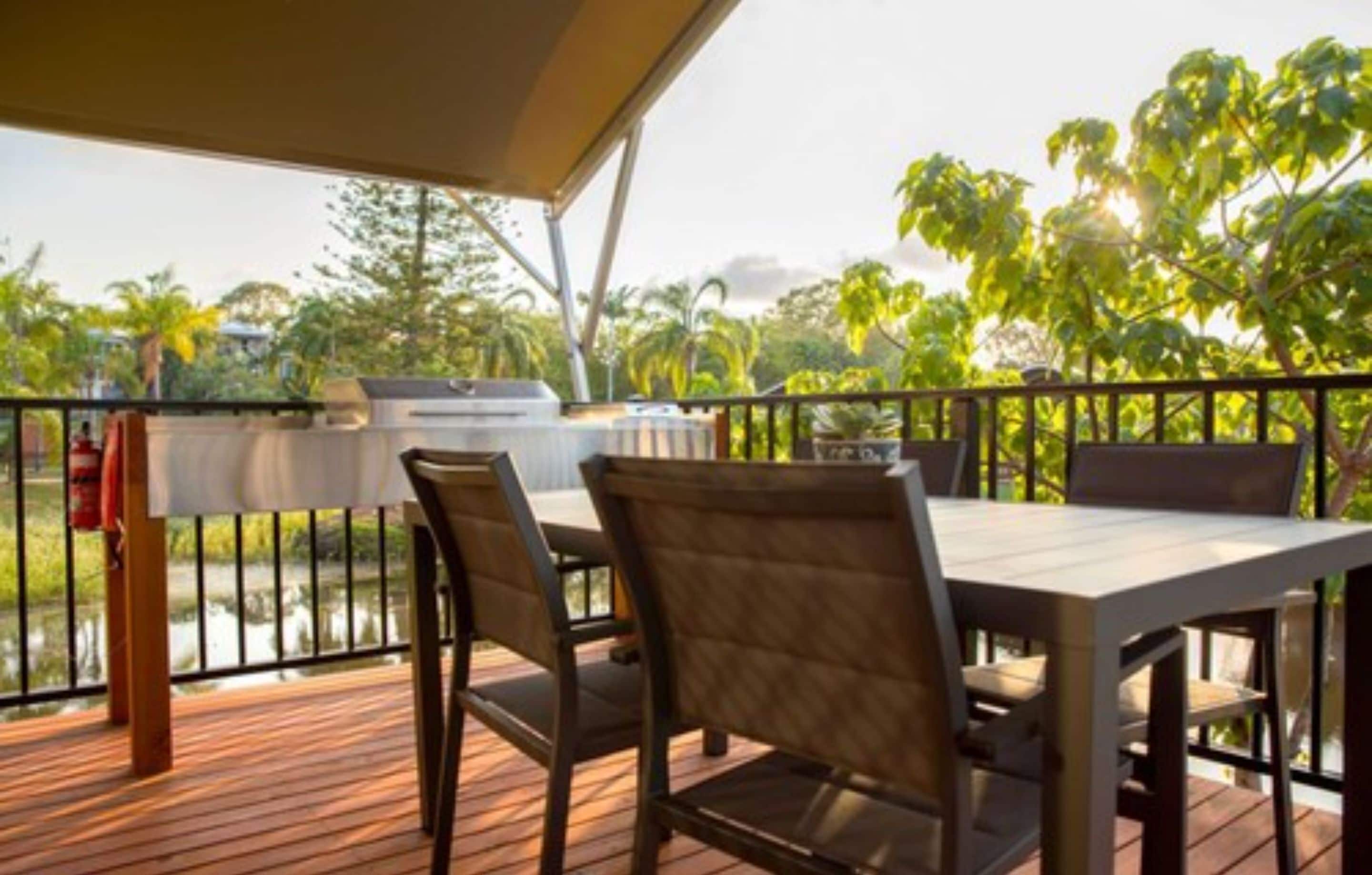 An outdoor patio with a grill, wooden deck, and chairs.