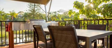 An outdoor patio with a grill, wooden deck, and chairs.