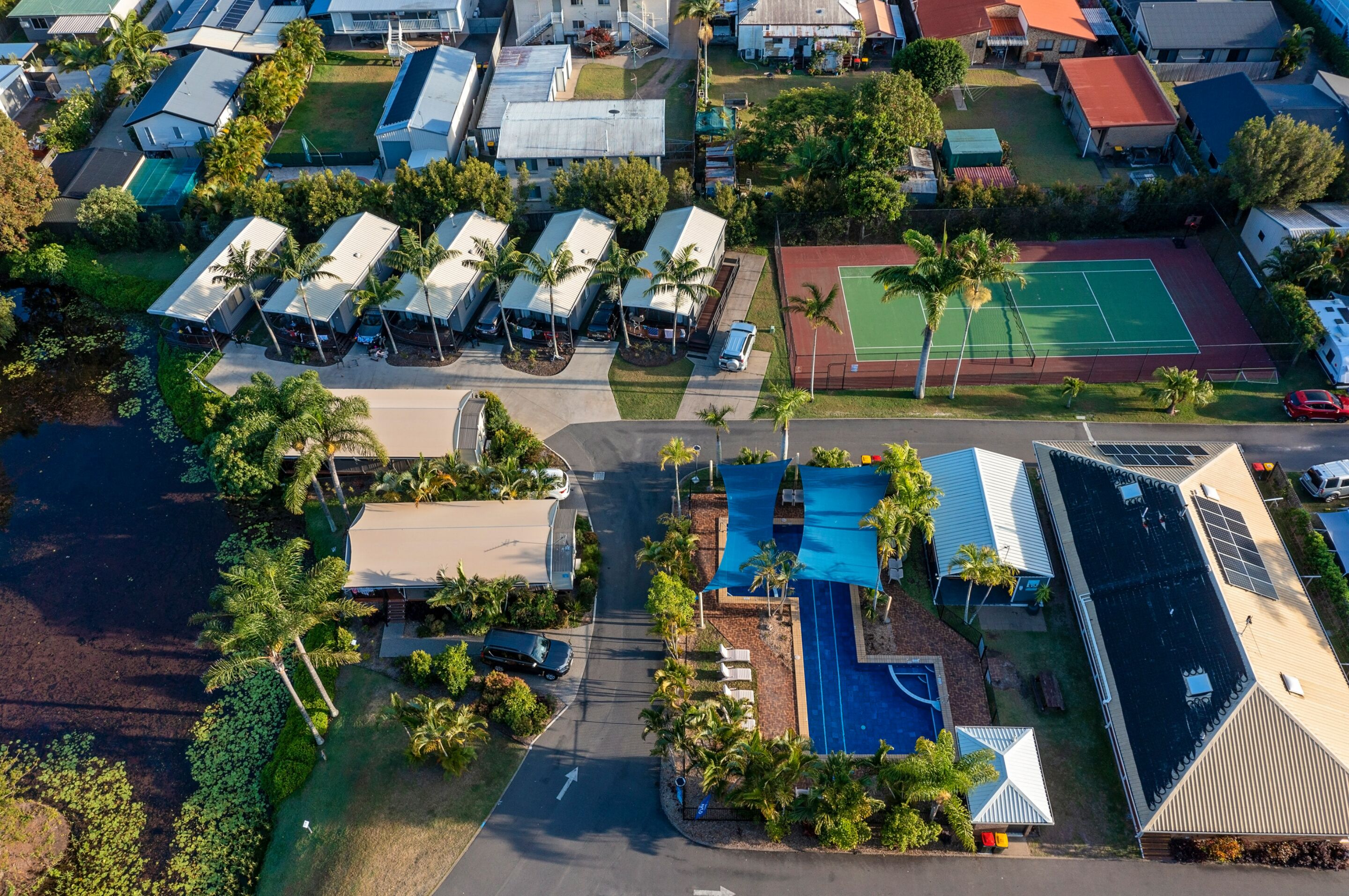 Vista aérea de una zona residencial con varias casas, una cancha de tenis y una piscina.