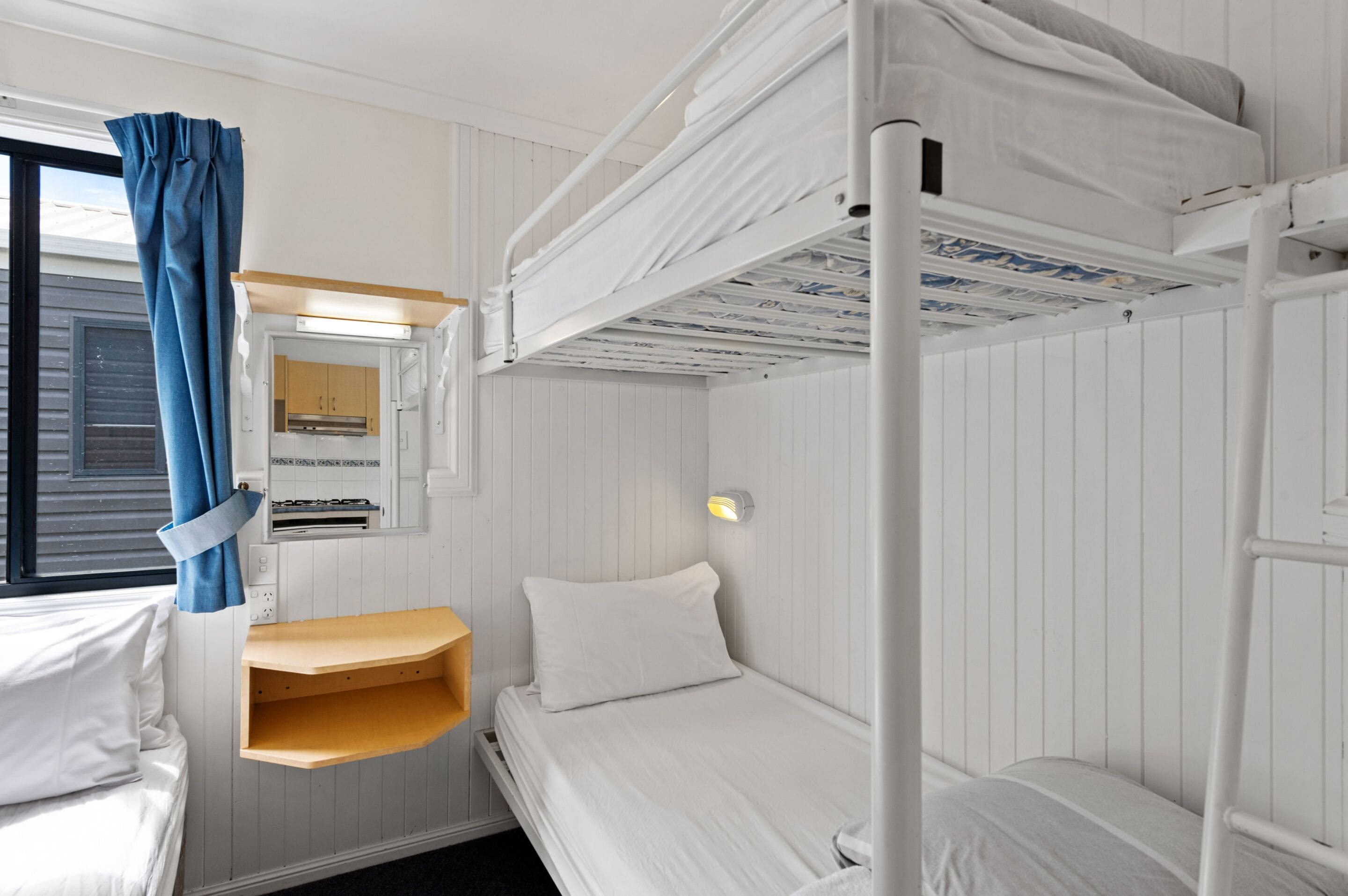 A bunk bed room with a window, a small shelf, and a wall-mounted light fixture.