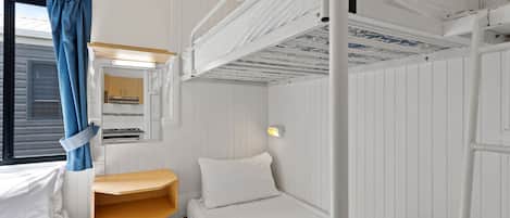 Une chambre avec un lit superposé, une fenêtre, une petite étagère et un luminaire fixé au mur.