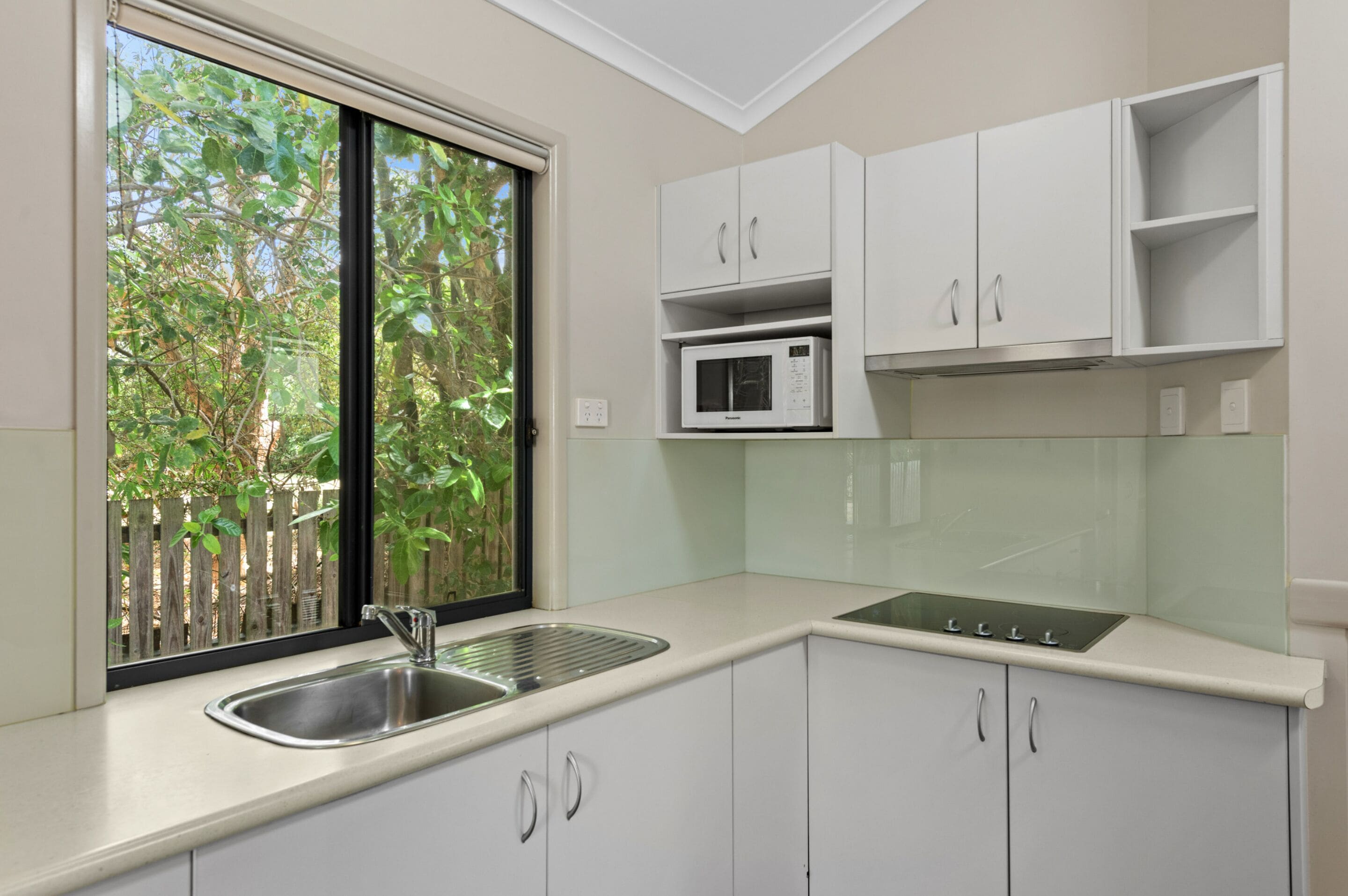 Cucina con pensili bianchi, lavello in acciaio inossidabile, forno a microonde e finestra vista alberi.