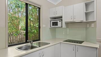 Cucina con pensili bianchi, lavello in acciaio inossidabile, forno a microonde e finestra vista alberi.