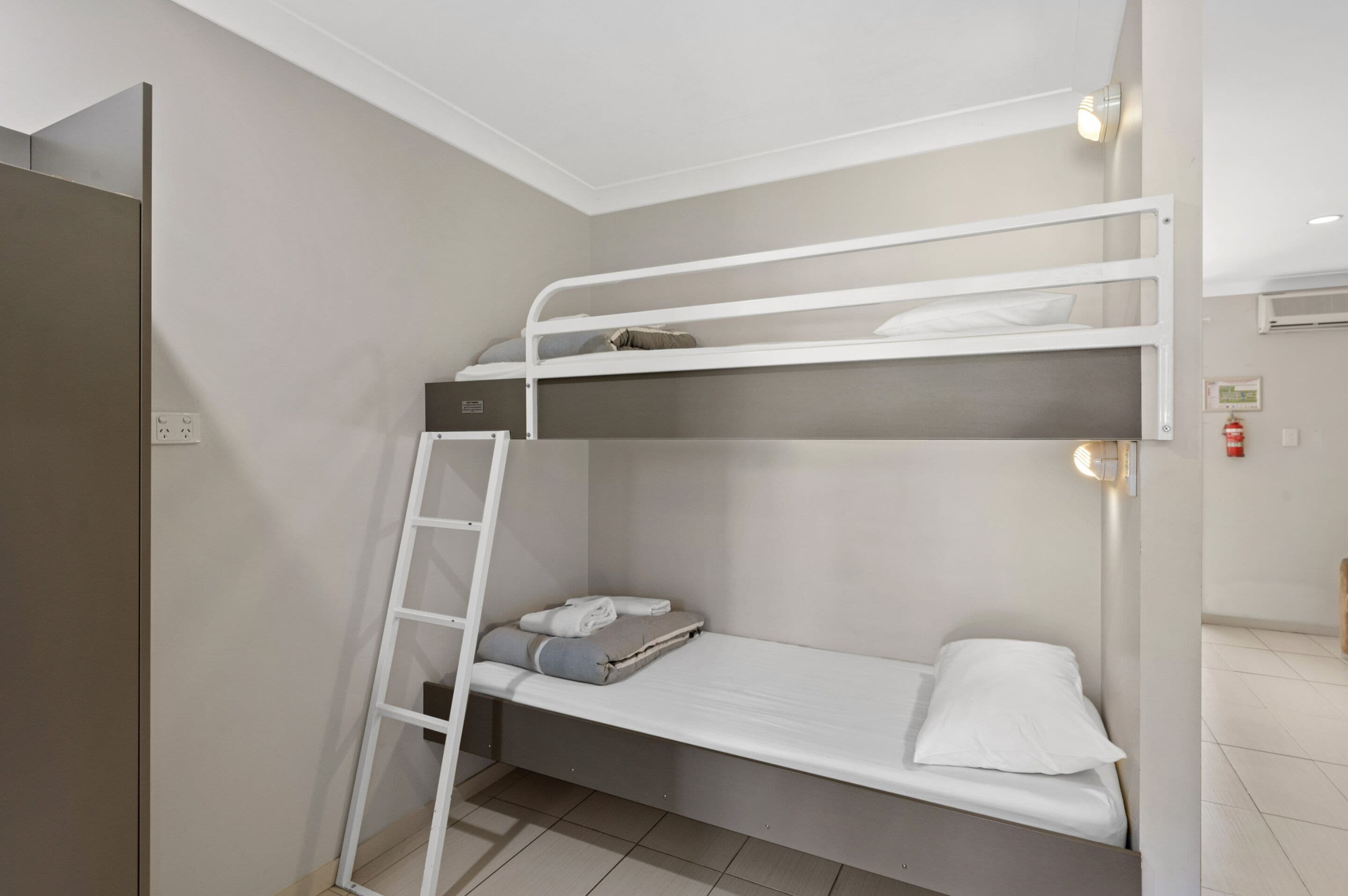 A bunk bed with a ladder, a small shelf, and a white wall.