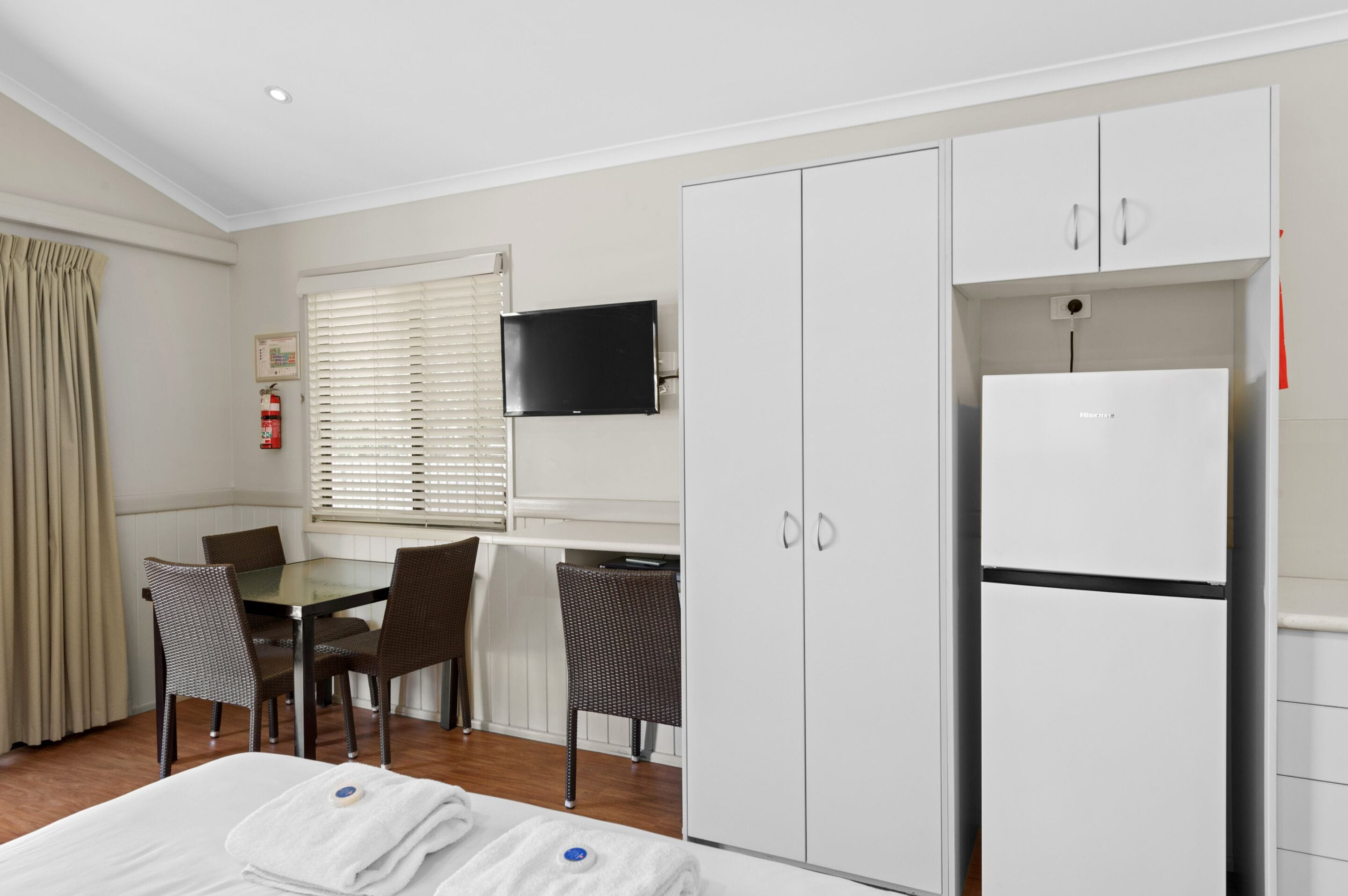 Una habitación de hotel con cama, una mesa de comedor con sillas, televisión y refrigerador.