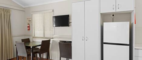 Una habitación de hotel con cama, una mesa de comedor con sillas, televisión y refrigerador.