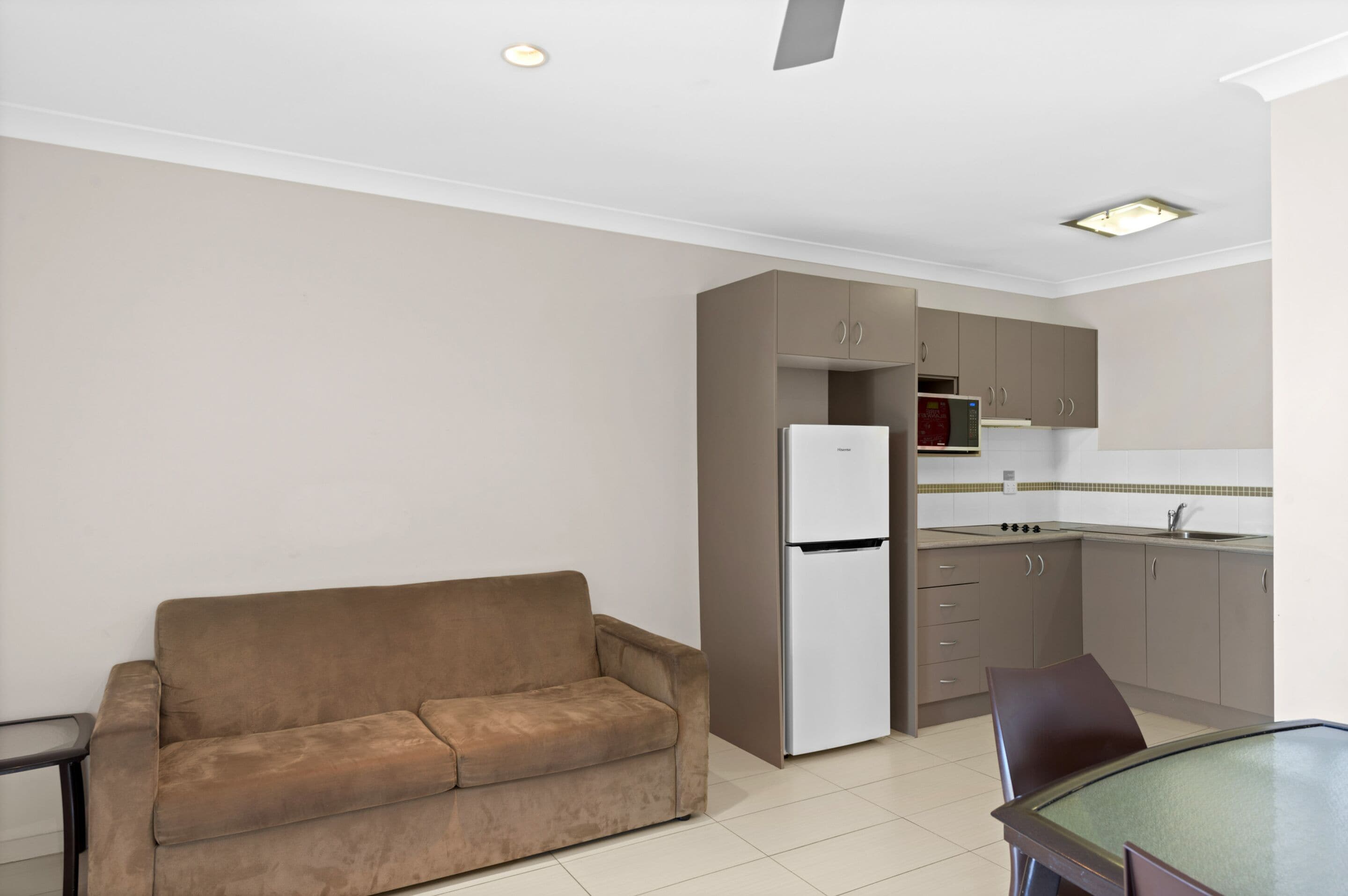 A compact living space with a sofa, a dining table, and a kitchenette area including a refrigerator and cabinets.
