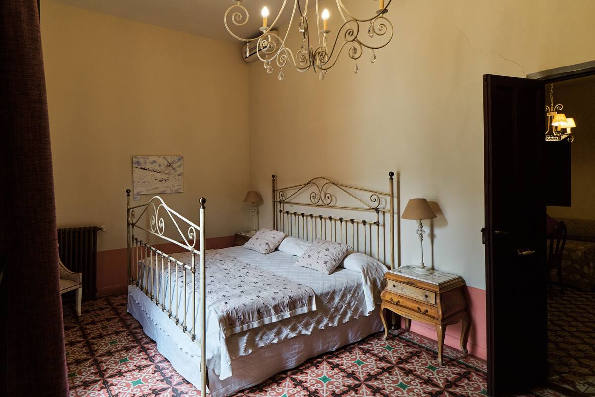 A bedroom with a metal bed frame, a bedside table with a lamp, a chair, and a patterned floor.
