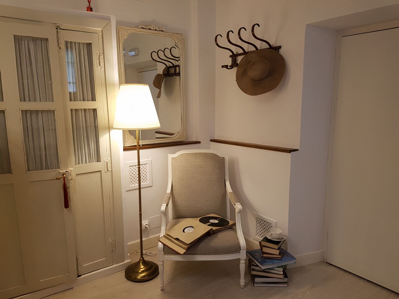A room with a white door, a chair with a CD case, a lamp, and a hat on the wall.