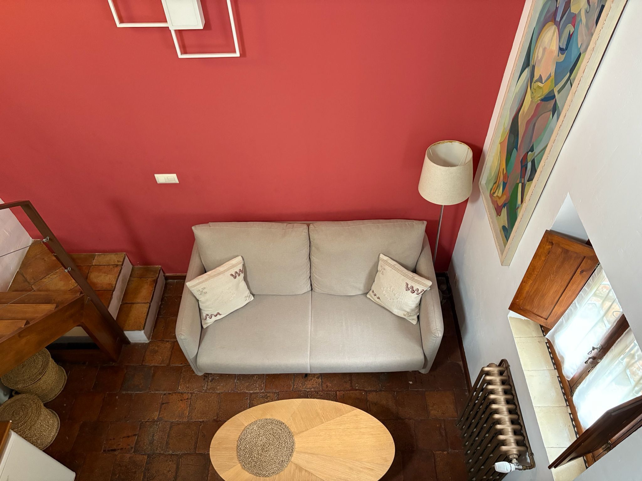 Una sala de estar con un sofá, una mesa redonda de madera, un radiador y una escalera.