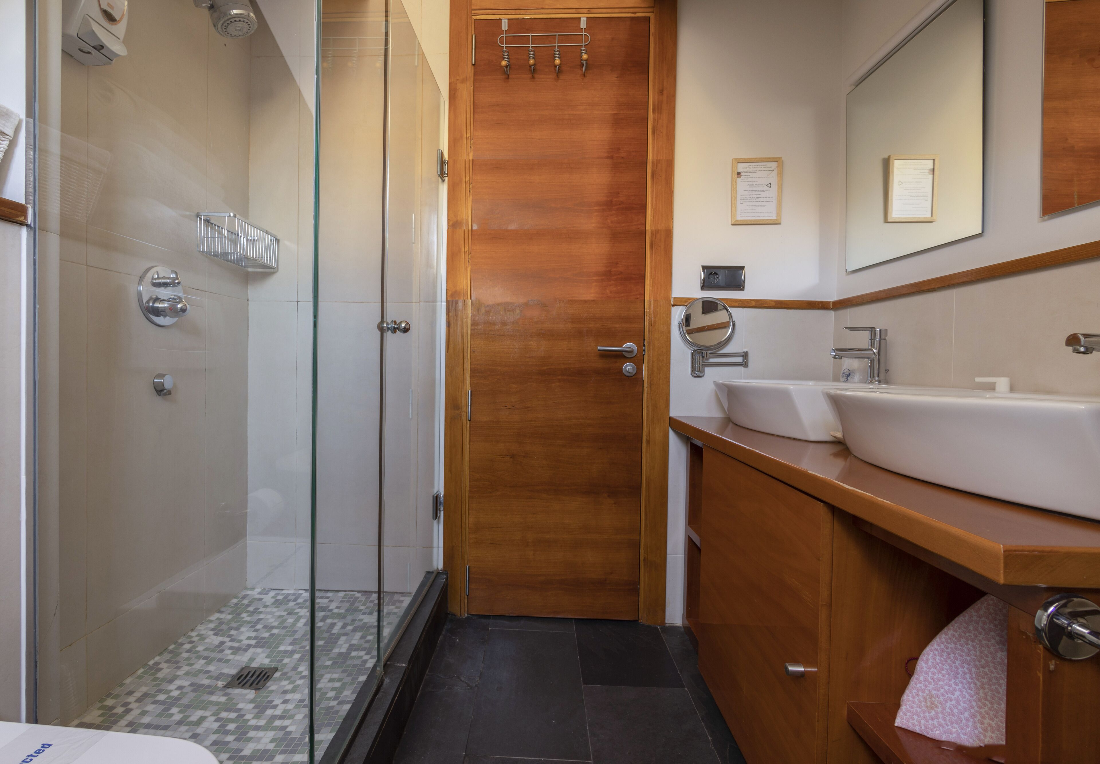A modern bathroom with a glass shower enclosure, a wooden door, a sink with a mirror, and a towel rack.
