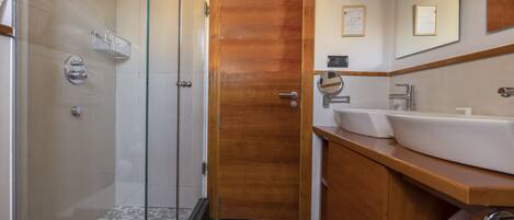 A modern bathroom with a glass shower enclosure, a wooden door, a sink with a mirror, and a towel rack.