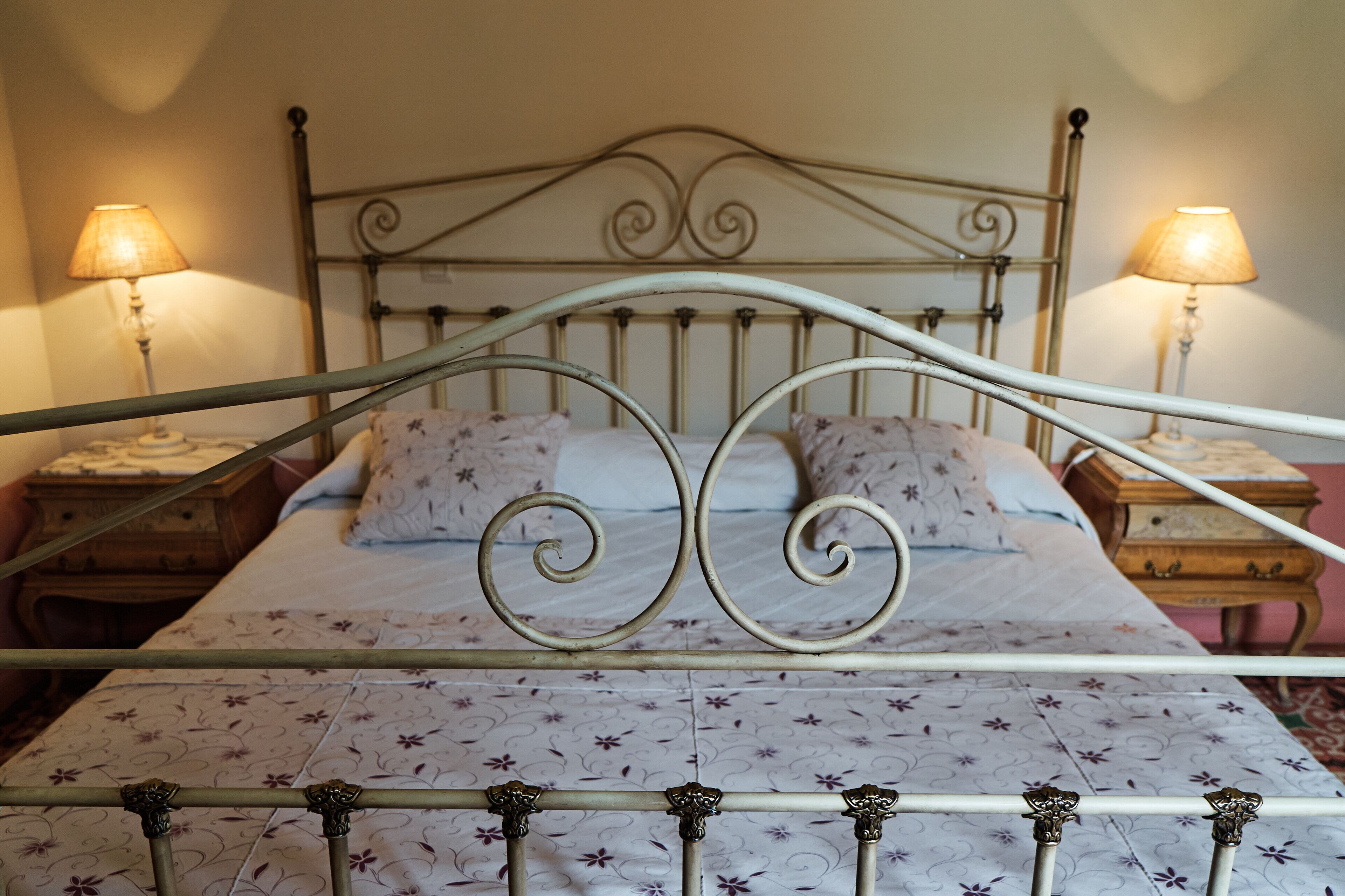 Una cama con estructura metálica, dos mesitas de noche y dos lámparas.