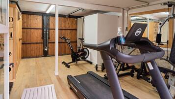 Een fitnessruimte met trainingsapparatuur, waaronder een loopband, een hometrainer en een gewichtbank.
