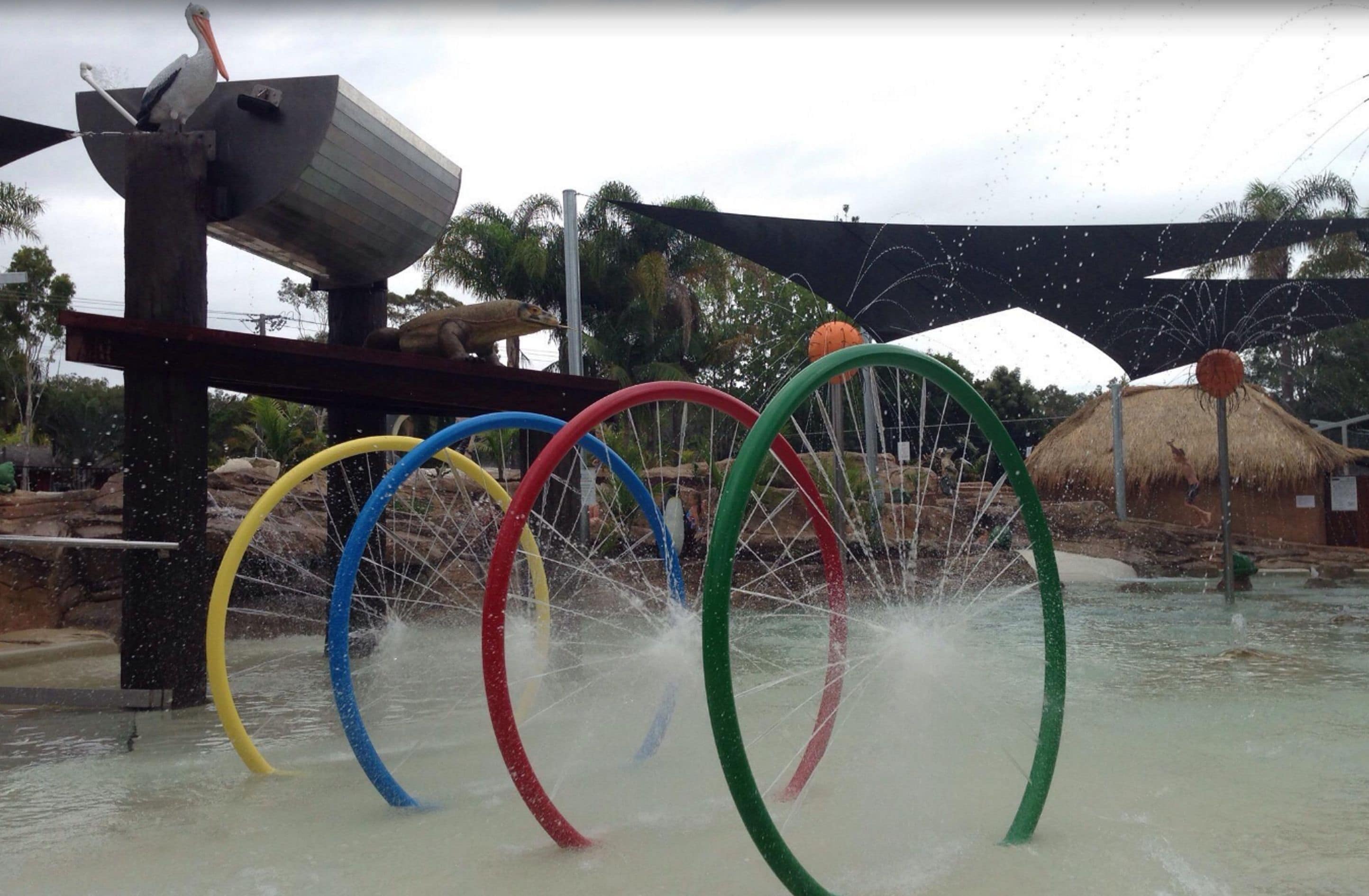 A water play area with colorful rings and a pelican sculpture.