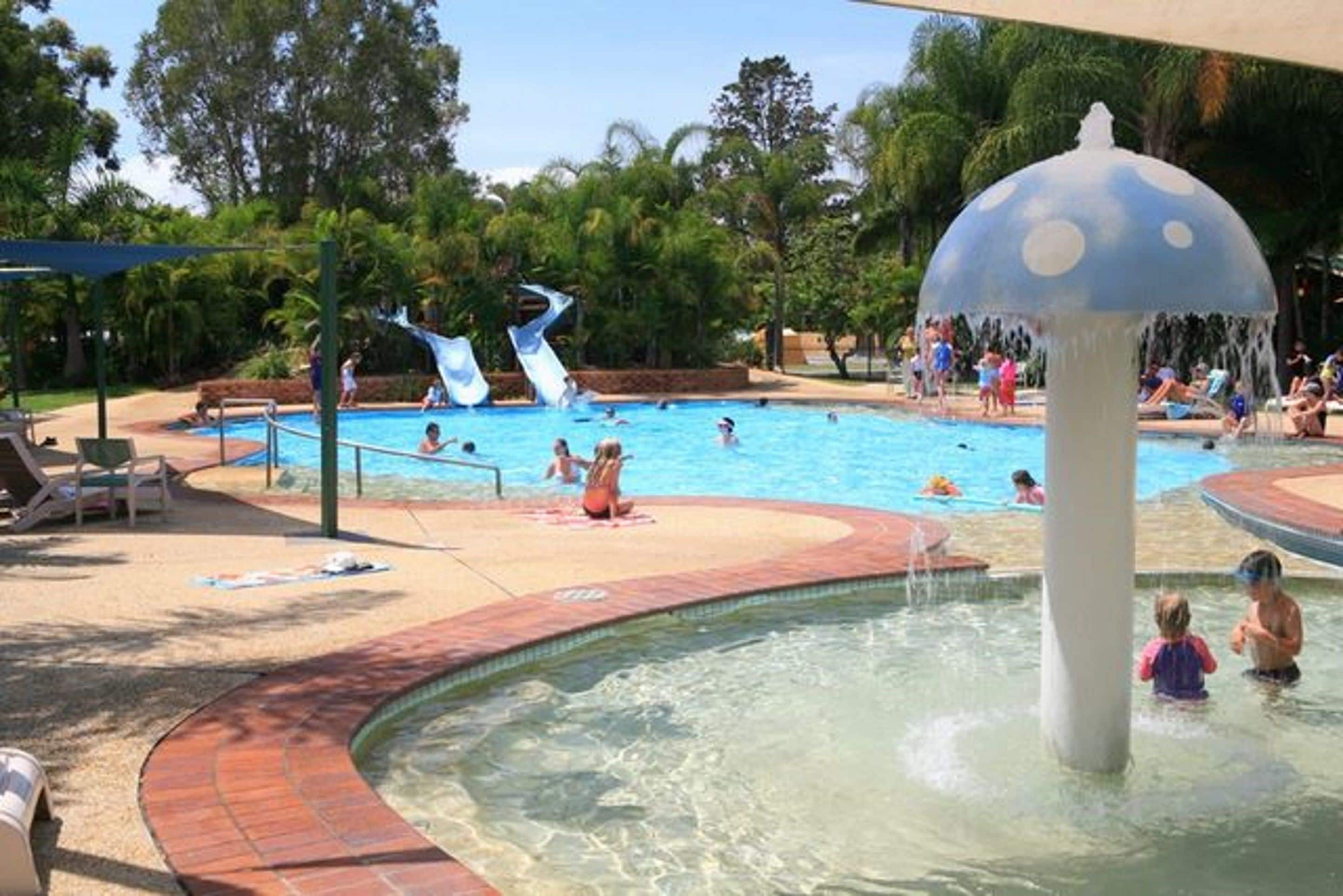 A swimming pool area with a water slide and a mushroom-shaped water feature.