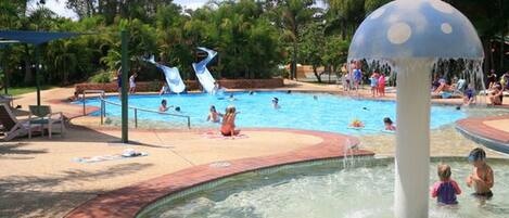 A swimming pool area with a water slide and a mushroom-shaped water feature.
