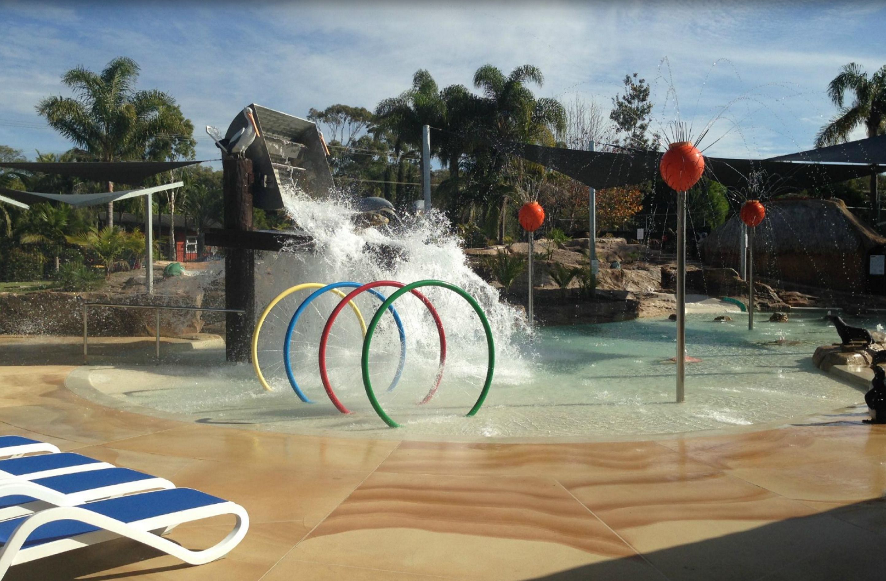 A water play area with a splash feature, a pool, and lounge chairs.