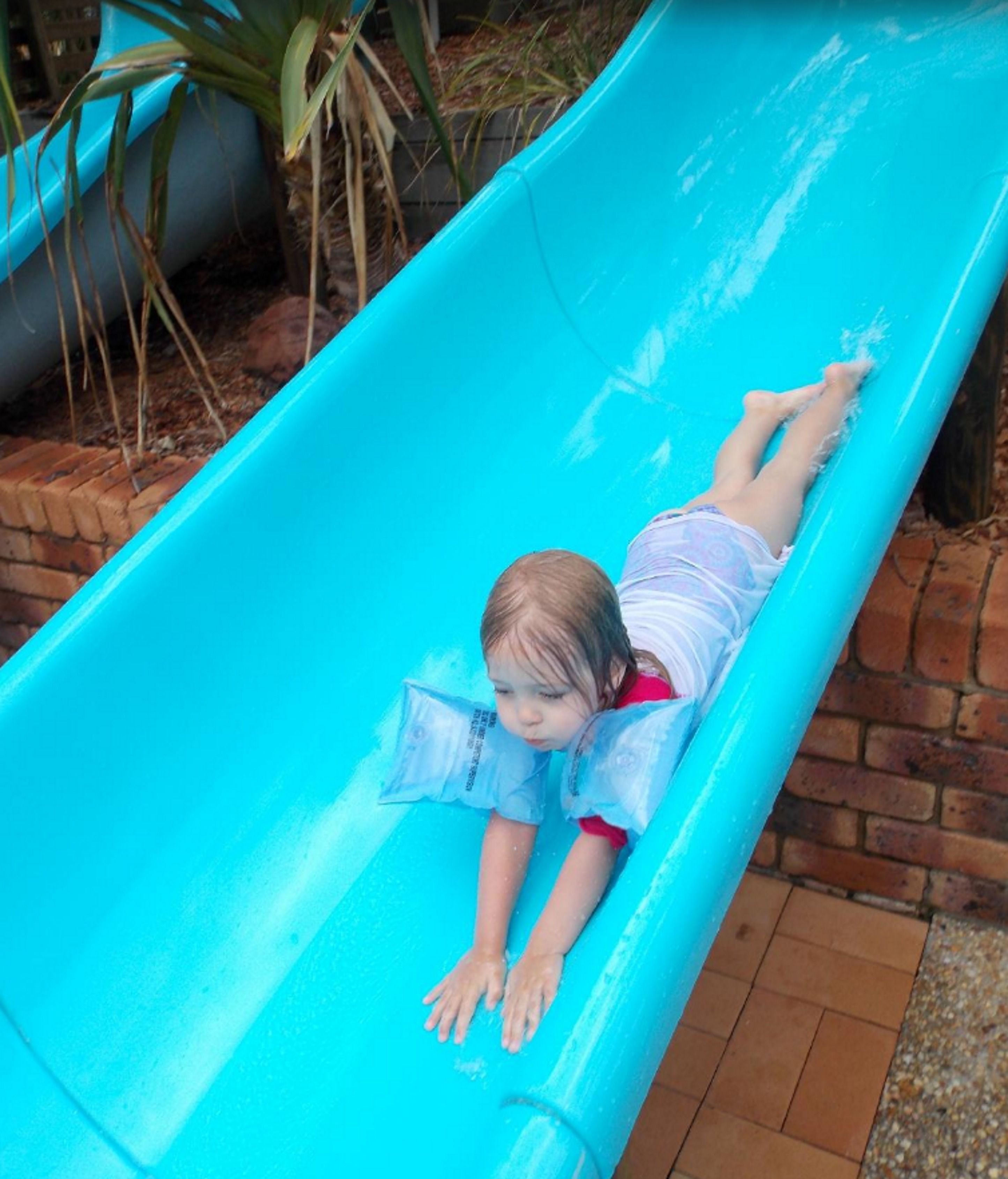 A child lying on a blue slide in an outdoor setting.