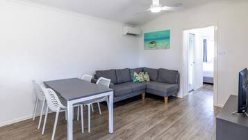 A modern living room with a grey sectional sofa, a white dining table with chairs, and a ceiling fan.