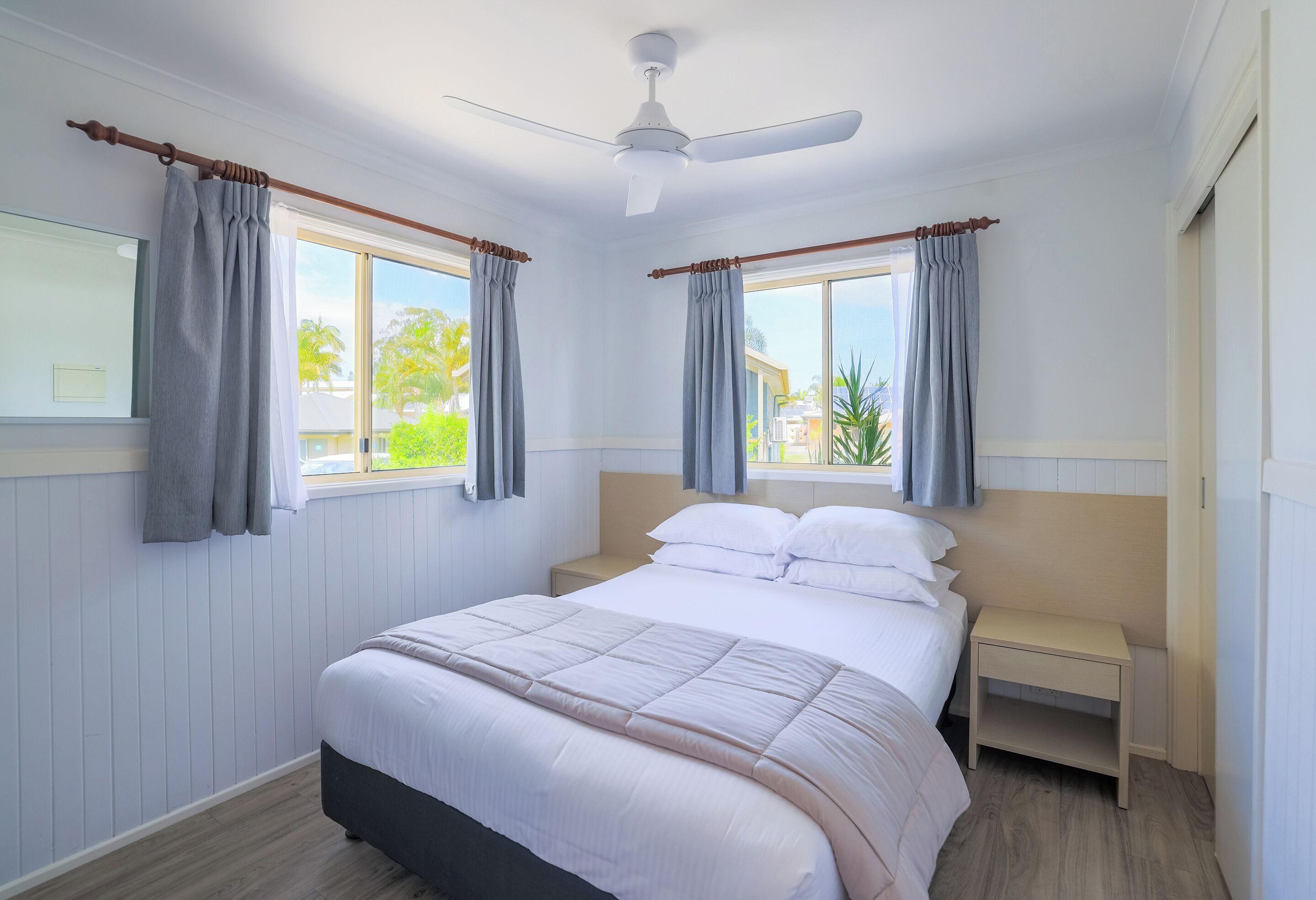 A bedroom with a bed, a nightstand, a ceiling fan, and curtains on two windows.