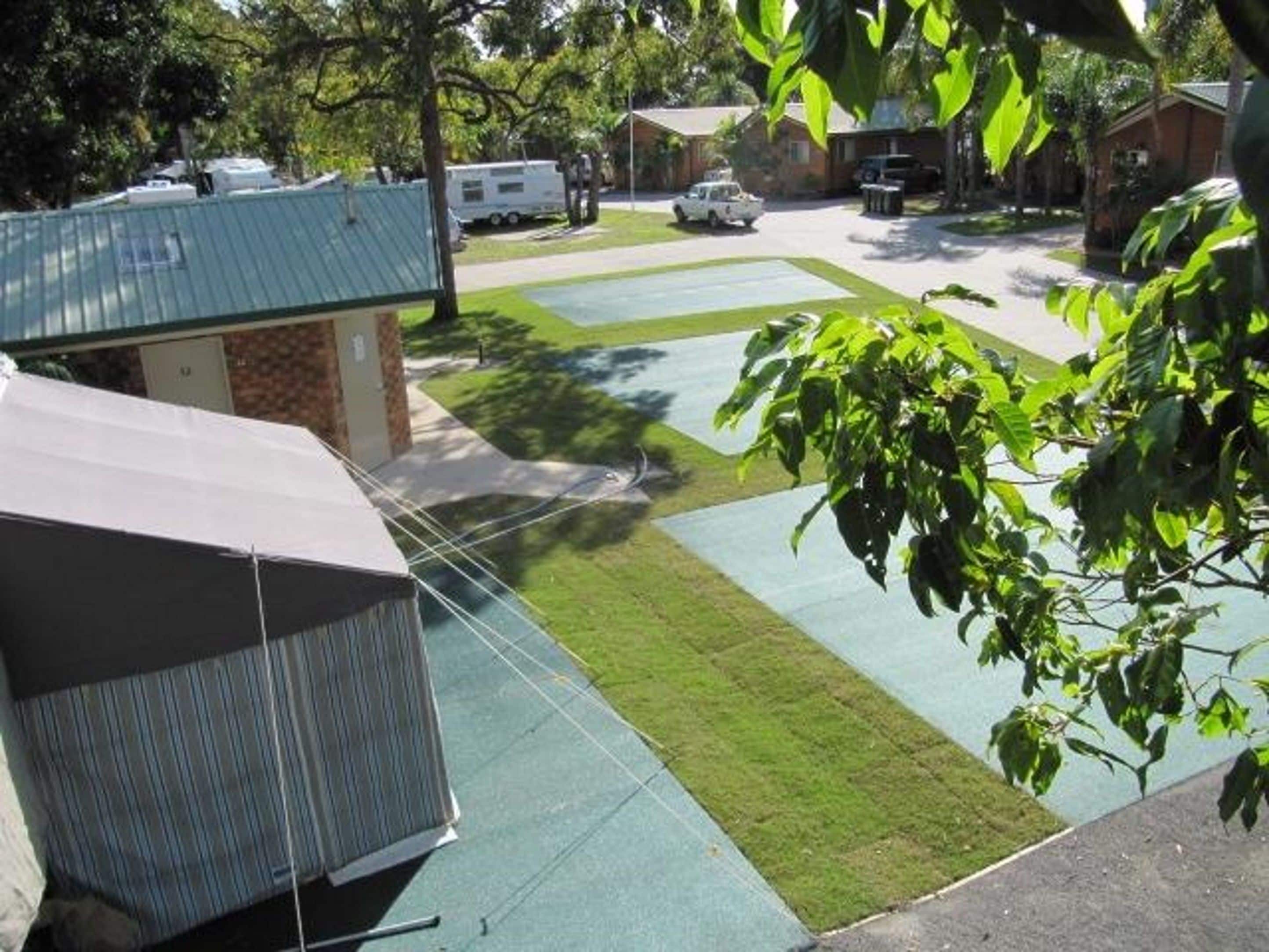 Un barrio residencial con césped verde, un pequeño edificio con base de ladrillo y techo de metal, y una camioneta blanca estacionada.
